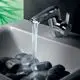 Chromene Waschtischarmatur von Ideal Standard mit Wasserfall-Austritt, montiert über einem Waschbecken, das mit dunklen Steinen gefüllt ist.